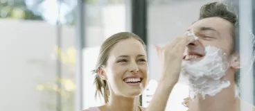 Un couple se taquine le matin face au miroir de la salle de bain.