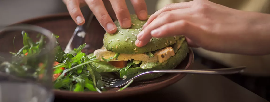 Une personne mangeant un hamburger végatal.